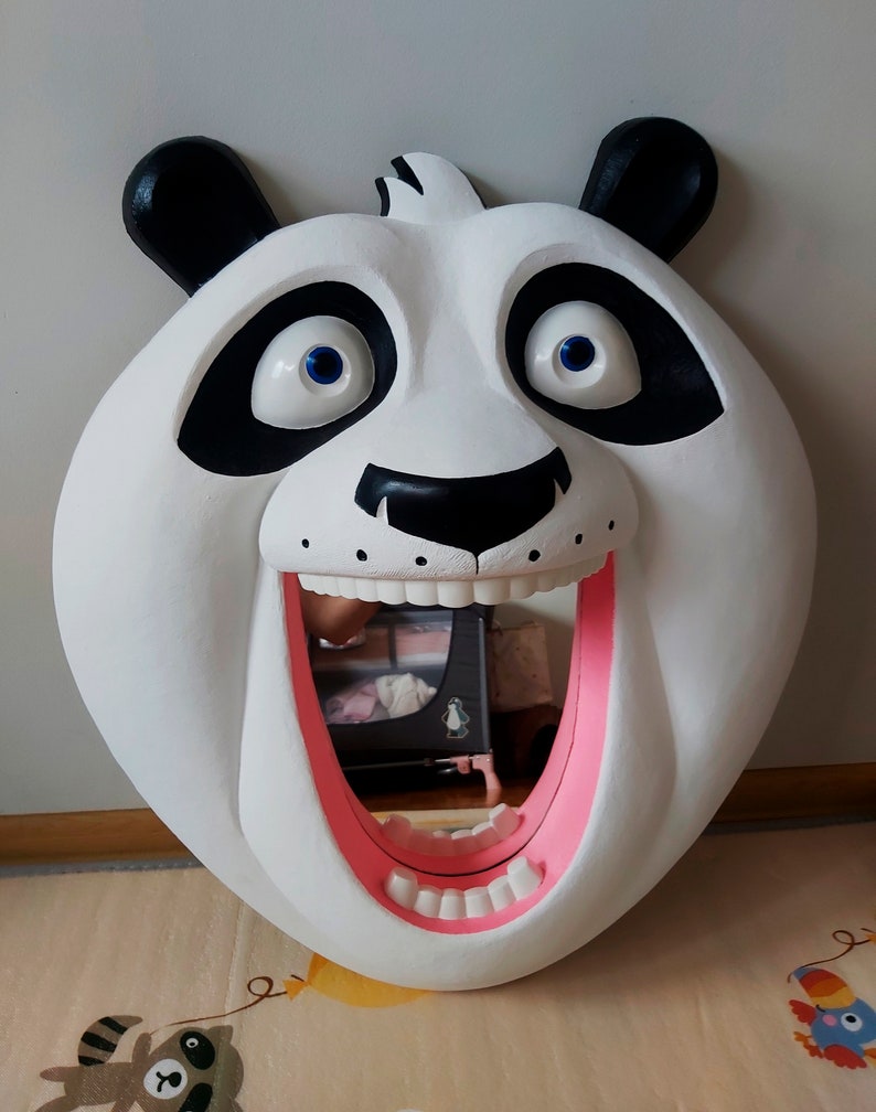 Puede incluir: Un gran espejo con forma de oso panda blanco, con orejas y parches en los ojos negros. El panda tiene una boca ancha y abierta con detalles internos rosas y dientes blancos. Los ojos son azules. El espejo est&aacute; dise&ntilde;ado para que parezca que el panda est&aacute; sonriendo.