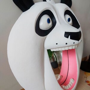 Puede incluir: Una gran escultura de cabeza de panda blanca con orejas y marcas oculares negras. La boca del panda est&aacute; abierta, revelando una lengua rosa y dientes blancos. Los ojos son azules. La escultura est&aacute; montada en una pared.