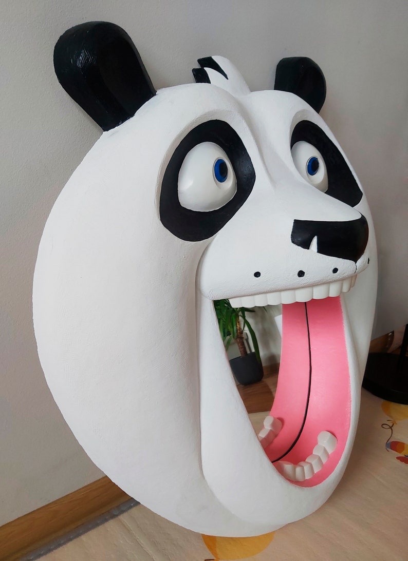 Puede incluir: Una gran escultura de cabeza de panda blanca con orejas y marcas oculares negras. La boca del panda est&aacute; abierta, revelando una lengua rosa y dientes blancos. Los ojos son azules. La escultura est&aacute; montada en una pared.