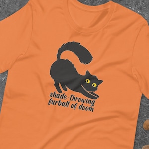 May include: Orange t-shirt with a black cat silhouette and the text "shade-throwing furball of doom".