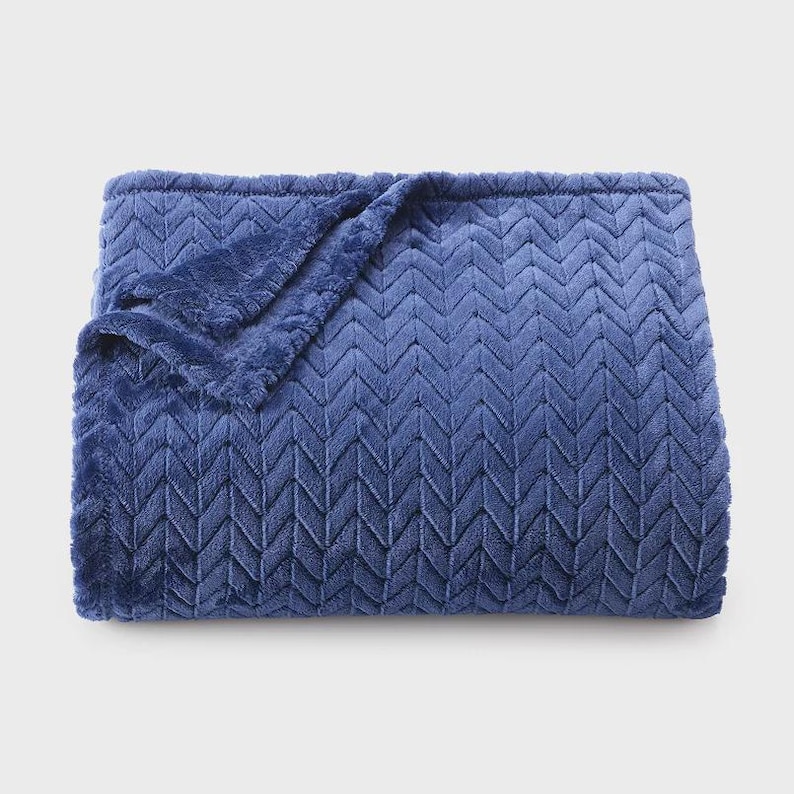 May include: A plush, blue blanket with a chevron pattern. The blanket is folded, with a corner turned down, revealing the soft texture. The color is a deep, rich blue, and the material appears to be a soft, fuzzy fabric.