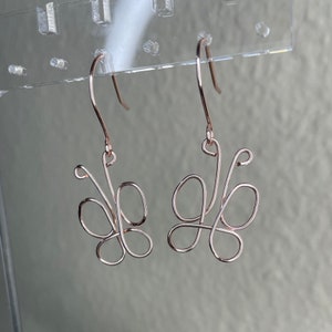 May include: A pair of rose gold butterfly earrings. The earrings are made of wire and are shaped like butterflies. The earrings are hanging from a clear plastic display card.