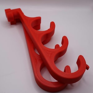 May include: A bright red plastic organizer rack featuring four curved hooks arranged in a vertical row. The structure has a mounting bracket at the top end and a series of circular cutouts along the main body, designed for hanging multiple items.