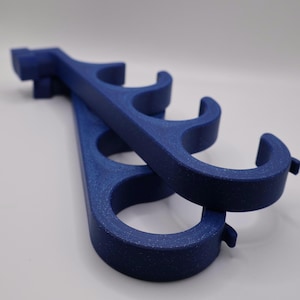 May include: Two dark blue, speckled, 3D-printed plastic hangers featuring a series of four circular openings along the length of each piece. The hangers have a curved hook design at one end and a flat, rectangular mounting tab at the other end.