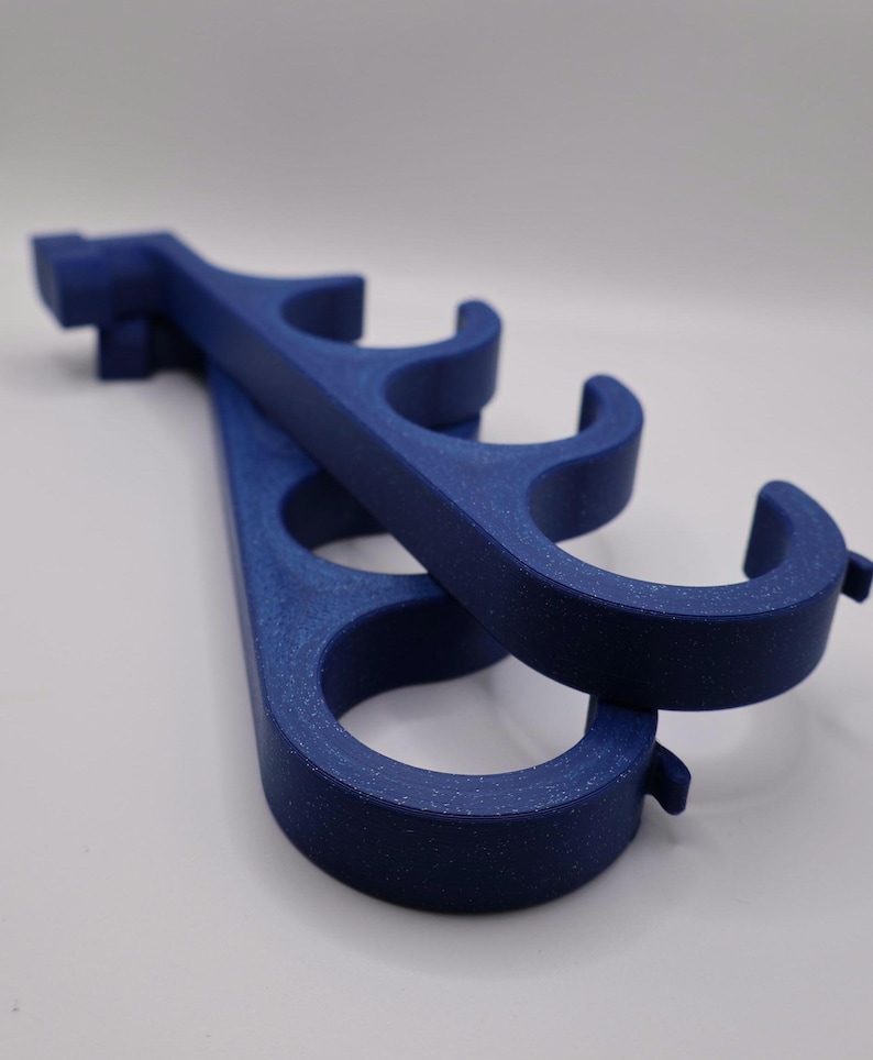May include: Two dark blue, speckled, 3D-printed plastic hangers featuring a series of four circular openings along the length of each piece. The hangers have a curved hook design at one end and a flat, rectangular mounting tab at the other end.