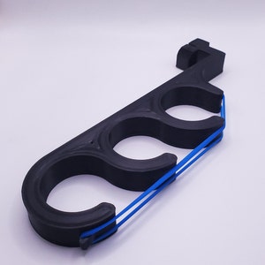 May include: A black, elongated, rigid plastic tool featuring three circular openings arranged in a row. A thin, bright blue elastic band is stretched across the front of the three circular openings, secured by small notches at each end of the frame.