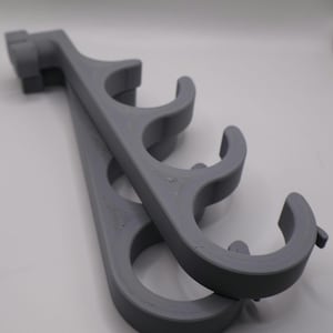 May include: A pair of matte gray 3D-printed wall-mounted storage racks, each featuring four curved, open-ended circular hooks arranged in a vertical row, designed to hold cylindrical items securely in place against a flat surface.