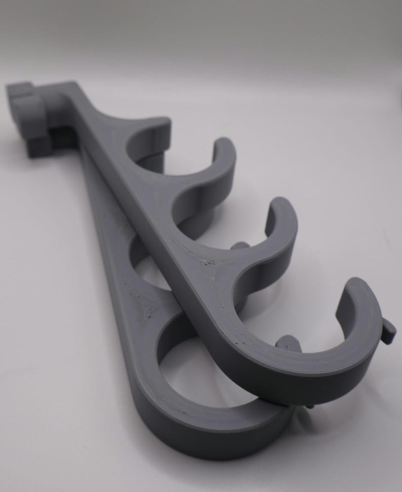 May include: A pair of matte gray 3D-printed wall-mounted storage racks, each featuring four curved, open-ended circular hooks arranged in a vertical row, designed to hold cylindrical items securely in place against a flat surface.