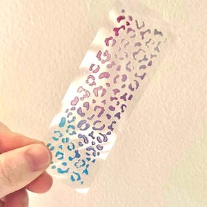 May include: A sheet of clear vinyl with a repeating pattern of iridescent blue, purple, and pink leopard spots.
