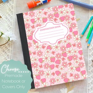 Könnte beinhalten: Ein rosa Notizbuch mit einem Blumen- und Erdbeermuster. Der Einband zeigt Gänseblümchen, Erdbeeren und Schmetterlinge. Der Text "COMPOSITION BOOK" wird in einem weißen Etikett angezeigt. Stifte und Schreibwaren umgeben das Notizbuch.