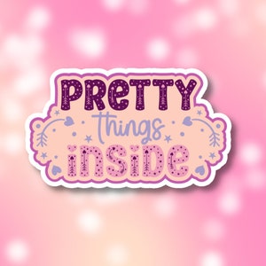 May include: A sticker with the words "PRETTY things INSIDE" in a decorative font. The text is in purple and pink, with star and heart accents. The sticker has a white border and is set against a pink background.