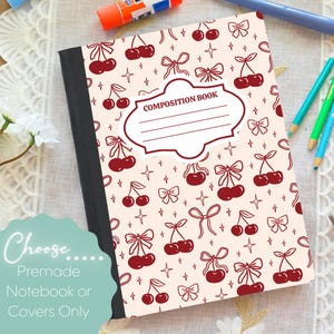 Pode incluir: Um caderno de composição com uma capa creme com um padrão de cerejas e laços bordô. A capa tem um rótulo branco que diz "COMPOSITION BOOK". Lápis e uma cola em bastão no fundo.