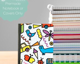 May include: A notebook with a colorful, whimsical design featuring a variety of cartoon illustrations, including a blue bird, a yellow car, and a butterfly. The cover has the text "Choose... Premade Notebook or Covers Only". A stack of notebooks is visible in the background.