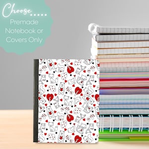 Puede incluir: Un cuaderno con lomo negro y cubierta blanca con un patrón repetido de corazones rojos, setas y animales del bosque. El texto "Choose... Premade Notebook or Covers Only" está en la esquina superior izquierda. Una pila de cuadernos está en el fondo.