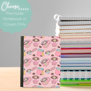 May include: A notebook with a pink cover featuring a pattern of coffee cups, coffee beans, and coffee scoops. The text "Choose... Premade Notebook or Covers Only" is in the upper left corner. A stack of notebooks is in the background.