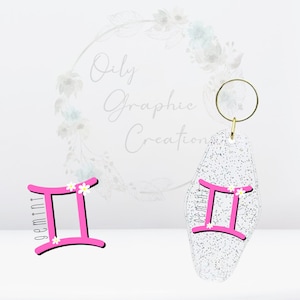 Op de afbeelding: Roze sleutelhanger met het sterrenbeeld Tweelingen, witte bloemen en glitter. De sleutelhanger is gevormd als een hotelsleutelhanger.