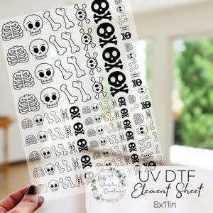 May include: A clear UV DTF element sheet featuring black and white skull and crossbones, rib cage, and bone designs. The sheet measures 8x11 inches and is held by a hand. The text "UV DTF Element Sheet" is visible.