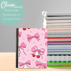 May include: A notebook with a pink cover featuring a pattern of pink bows and cherries on a light pink background. The notebook is shown next to a stack of other notebooks. Text on the image reads "Choose... Premade Notebook or Covers Only."