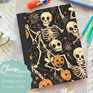 May include: A black notebook with a Halloween design. The cover displays a pattern of skeletons, pumpkins, and spiderwebs in orange and cream. The text "Choose... Premade Notebook or Covers Only" is on the bottom left.