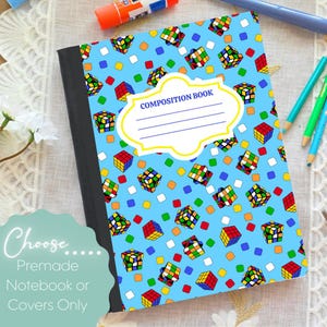 May include: A composition book with a light blue cover featuring a pattern of colorful Rubik's Cubes and small squares. The cover has a white label with the words "COMPOSITION BOOK" and lines for writing. The notebook has a black spine.