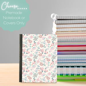 Peut inclure: Un cahier à motifs floraux avec une tranche noire est présenté devant une pile de cahiers. La couverture du cahier présente un fond crème avec des fleurs roses, bleues et vertes. Le texte de l'image se lit "Choose... Premade Notebook or Covers Only."