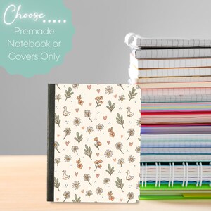 Puede incluir: Un cuaderno con una cubierta de color crema que presenta un patrón repetitivo de pequeñas margaritas blancas, flores naranjas, hojas verdes, corazones diminutos y patos blancos. Una pila de cuadernos se sitúa a la derecha del cuaderno principal.