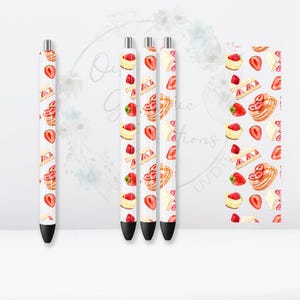 May include: Four white pens with a pattern of red strawberries and yellow pastry on them. The pens are on a white background.