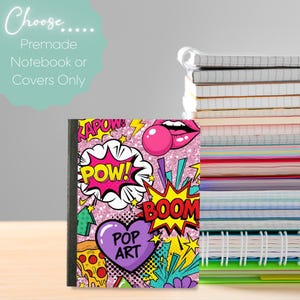 Könnte beinhalten: Ein Notizbuch mit einem Pop-Art-Design mit Sprechblasen im Comic-Stil mit Wörtern wie "POW!" und "BOOM!". Das Cover ist rosa mit Glitzereffekt und enthält ein lila Herz mit der Aufschrift "POP ART". Der Text "Choose... Premade Notebook or Covers Only" ist ebenfalls sichtbar.