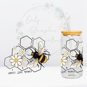 Könnte beinhalten: Ein klares Glas mit einem Bambusdeckel und einem wiederverwendbaren Strohhalm. Der Becher hat ein Bienen- und Wabenmuster mit dem Text "Sweet Like Honey". Das Design umfasst die Farben Gelb, Schwarz und Weiß.