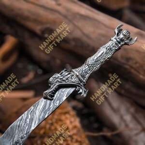 May include: A silver dragon sword with a detailed dragon head handle and a patterned blade. The sword is lying on a wooden surface.