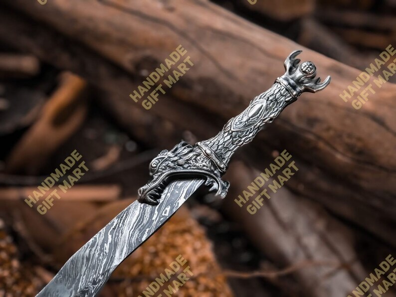 May include: A silver dragon sword with a detailed dragon head handle and a patterned blade. The sword is lying on a wooden surface.