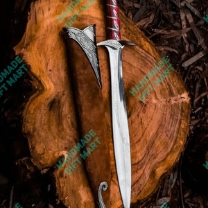 May include: A silver sword with a red and silver handle and a leather scabbard. The sword is on a wooden surface.