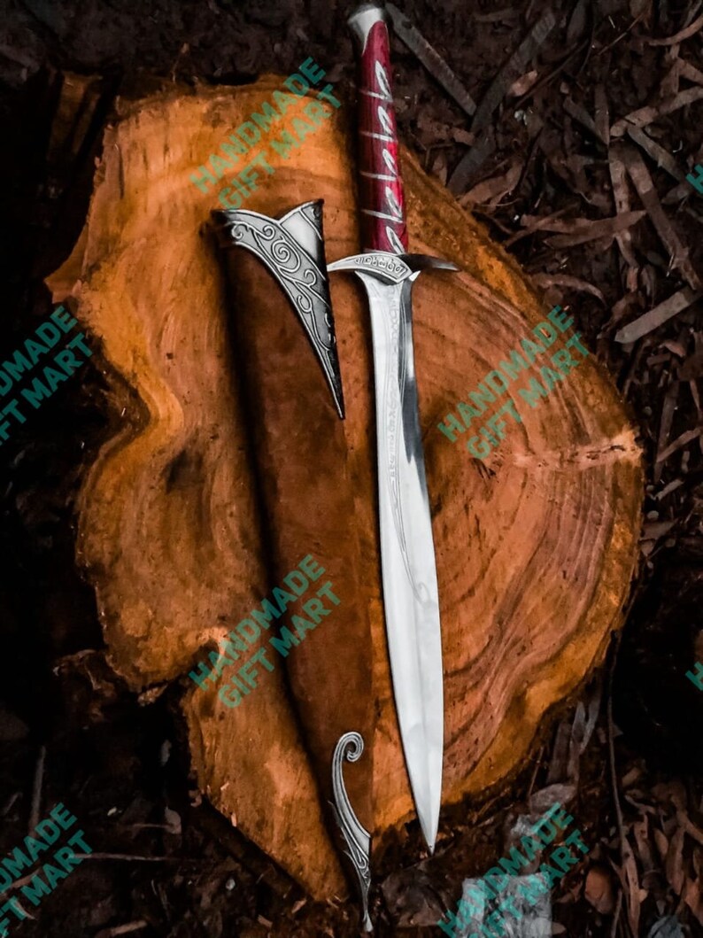May include: A silver sword with a red and silver handle and a leather scabbard. The sword is on a wooden surface.