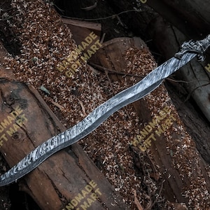 May include: A silver sword with a dragon head handle. The sword is made of Damascus steel and has a wavy pattern. The sword is lying on a wooden surface.