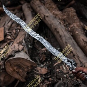 May include: A silver sword with a dragon head handle. The sword has a wavy pattern on the blade. The sword is held by a hand against a background of brown wood.