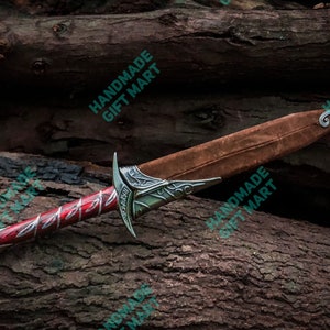 May include: A red and silver dagger with a brown leather sheath. The dagger has a decorative handle and a sharp blade. The sheath has a decorative metal tip.