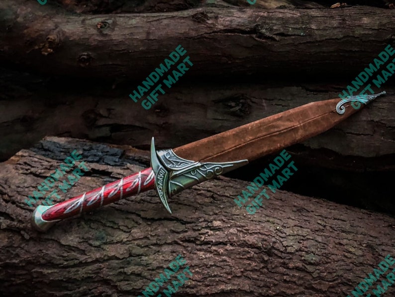 May include: A red and silver dagger with a brown leather sheath. The dagger has a decorative handle and a sharp blade. The sheath has a decorative metal tip.