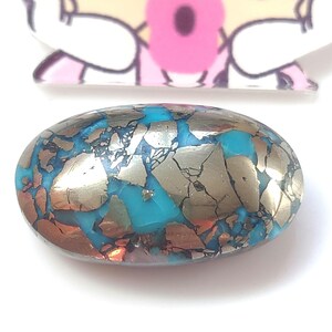 Peut inclure: Une pierre précieuse ovale en cabochon de couleur turquoise et or avec un motif marbré. La pierre précieuse a une surface lisse et polie.