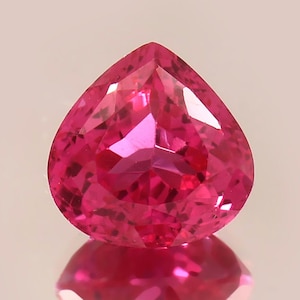 Peut inclure: Une pierre précieuse rose vif en forme de cœur avec une taille facetée. La pierre précieuse est placée sur un fond blanc.