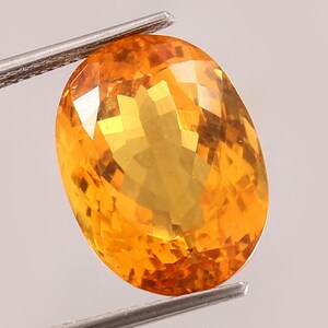 May include: A bright orange oval-shaped gemstone with a faceted cut. The gemstone is set in a silver setting.