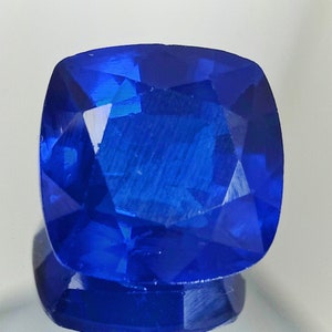 Könnte beinhalten: Ein tiefblauer Edelstein mit einem Kissen-Schliff. Der Edelstein hat eine facettierte Oberfläche und reflektiert Licht.