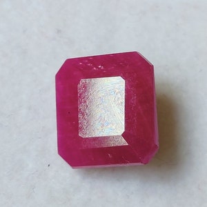 May include: A deep red emerald cut gemstone with a slightly irregular shape.