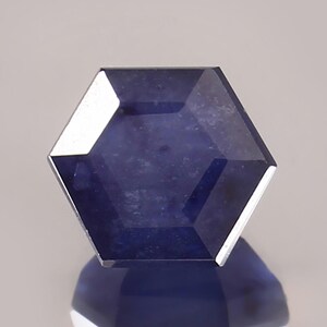 May include: A deep blue hexagonal gemstone with a faceted cut. The gemstone has a slightly cloudy appearance.