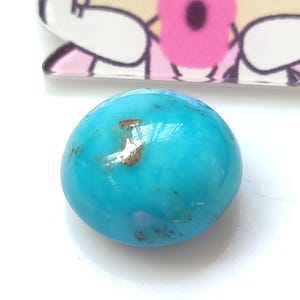 May include: A smooth, oval-shaped turquoise gemstone with a light blue color and brown and silver inclusions.