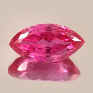 May include: A vibrant pink marquise-shaped gemstone with a faceted cut. The gemstone is reflecting light, showcasing its brilliance.