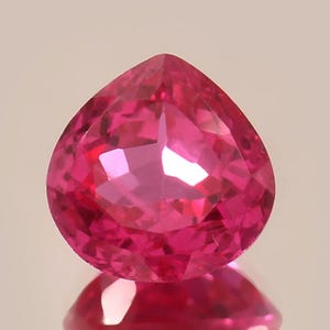 May include: A vibrant pink gemstone with a heart-shaped cut. The gemstone is faceted and has a high polish.