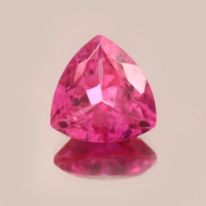 Peut inclure: Une pierre précieuse rose vif de forme triangulaire. La pierre est facetée et réfléchit la lumière.