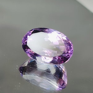 May include: A light purple oval-shaped amethyst gemstone with a faceted cut.