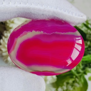 Peut inclure: Une pierre d'agate rose et blanche avec une surface lisse et polie. La pierre présente un motif naturel tourbillonnant de rose et de blanc.