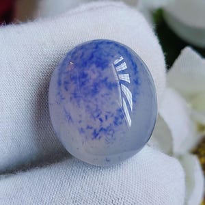 May include: A round, translucent, white cabochon with blue flecks throughout. The cabochon is smooth and polished.